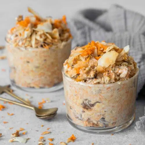 Two glass jars filled with creamy vegan bircher topped with grated carrot, walnuts and toasted coconut flakes