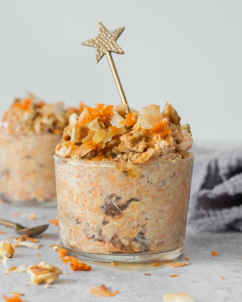 Two glass jars filled with creamy vegan bircher topped with grated carrot, walnuts and toasted coconut flakes