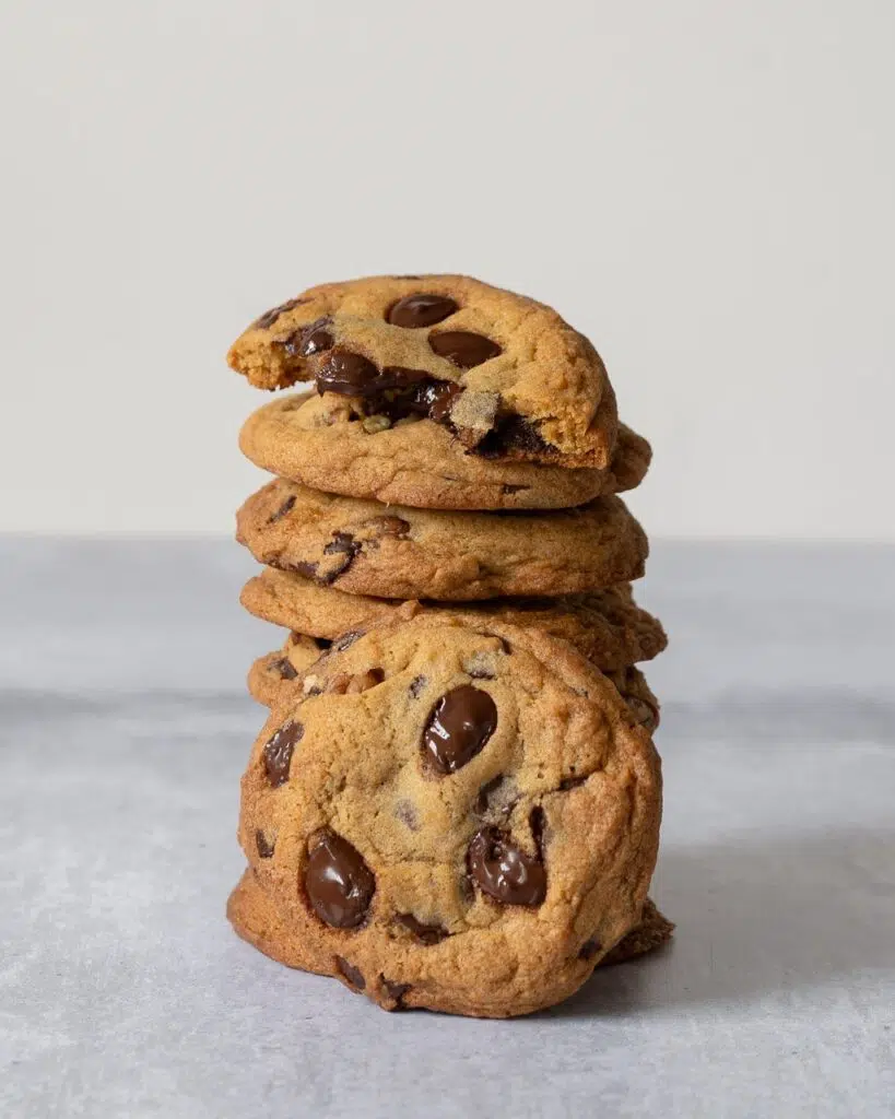 A stack of deliciously soft and chewy vegan cookies freshly baked with melty chocolate chips and caramelised pecan pieces