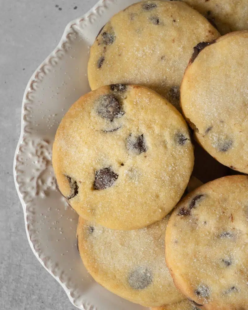 A plate of buttery vegan chocolate chip shortbread cookies, dusted in sugar.