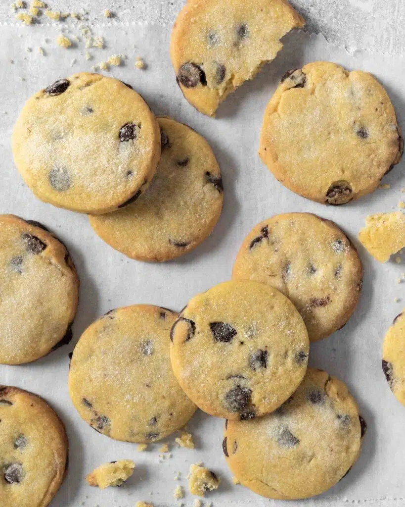 Buttery vegan chocolate chip shortbread cookies, dusted in sugar, resting on a table top.