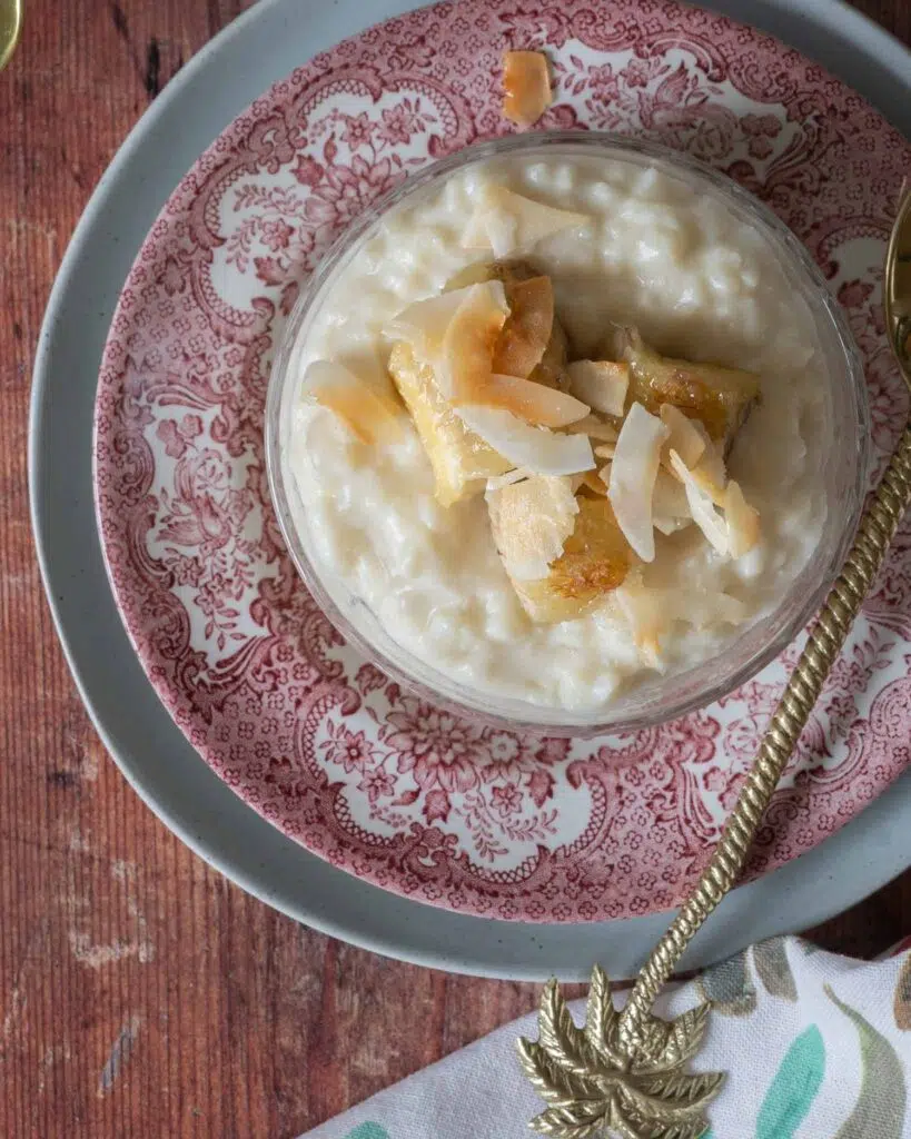A glass dish of creamy coconut rice pudding, topped with caramelised bananas and toasted coconut flakes.