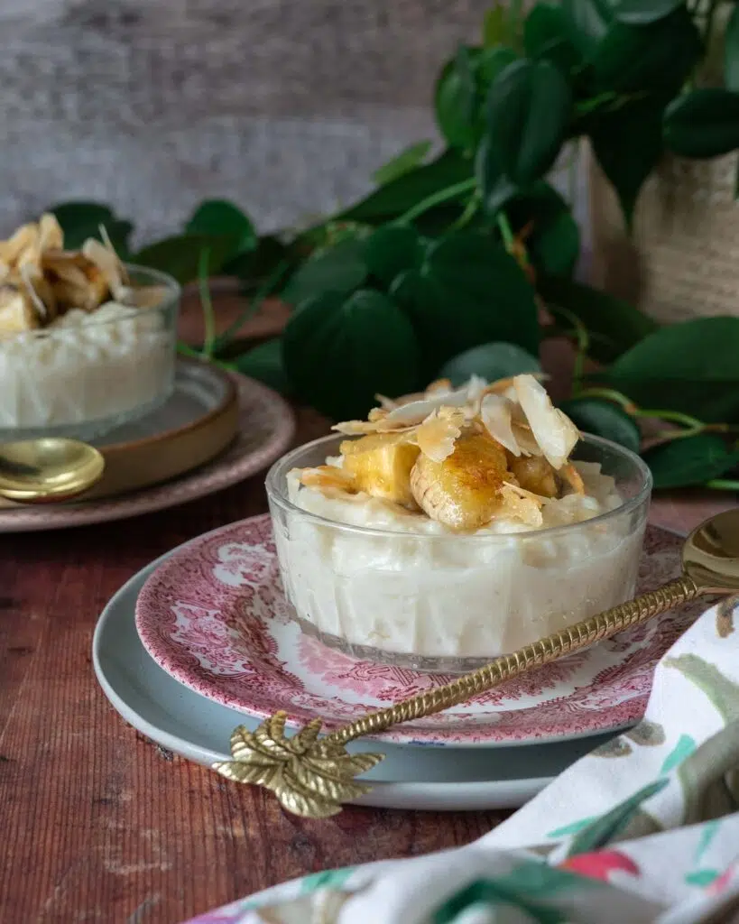 Two glass dishes of creamy coconut rice pudding, topped with caramelised bananas and toasted coconut flakes.