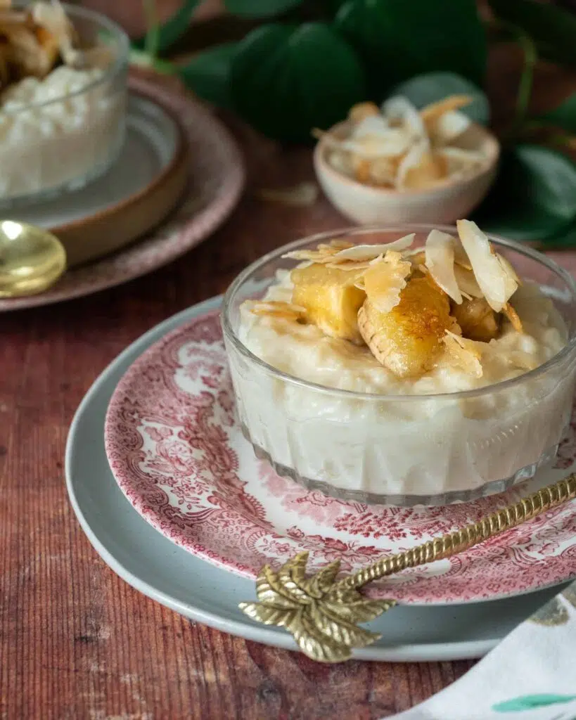 A glass dish of creamy coconut rice pudding, topped with caramelised bananas and toasted coconut flakes.
