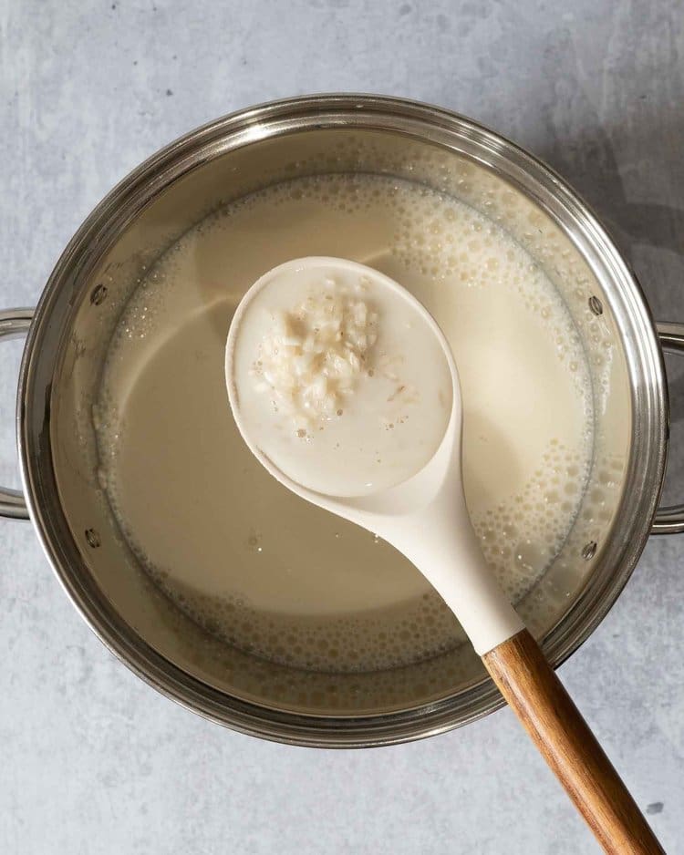 The ingredients for making coconut rice pudding in a saucepan with a spoonful of rice and coconut milk being scooped out