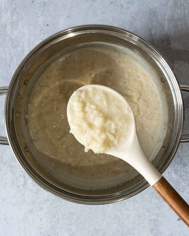 The ingredients for making coconut rice pudding in a saucepan with a spoonful of rice and coconut milk being scooped out