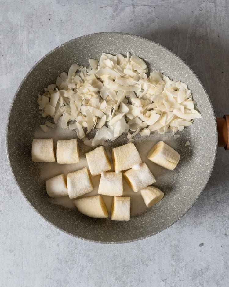 A non stick frying pan filled with coconut chips and banana chunks ready to be toasted and caramelised
