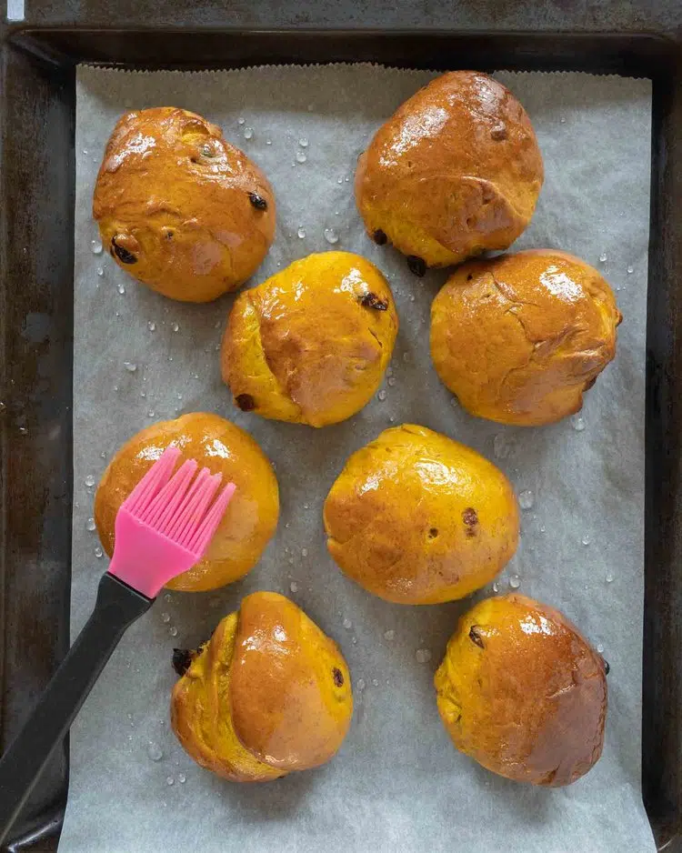 Cornish saffron buns fresh out of the oven being glazed with sugar glaze