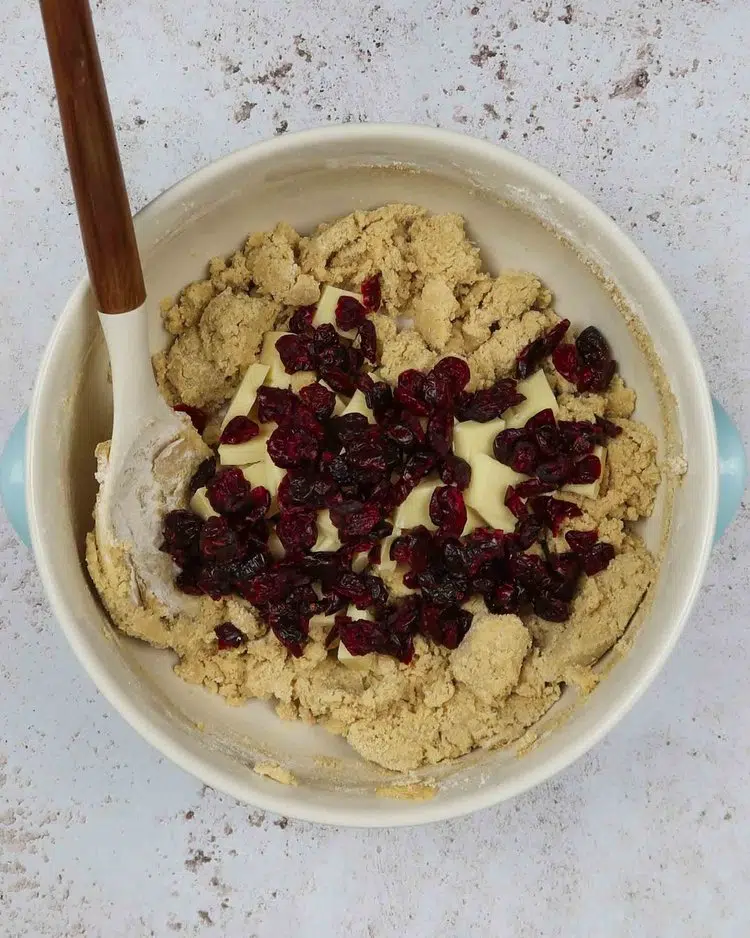 Dried cranberries and vegan white chocolate chunks added to a bowl of cookie dough ready to be mixed in