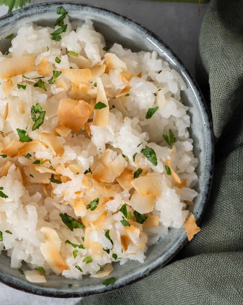 A bowl of fluffy white coconut rice topped with lightly toasted coconut flakes and fresh coriander.