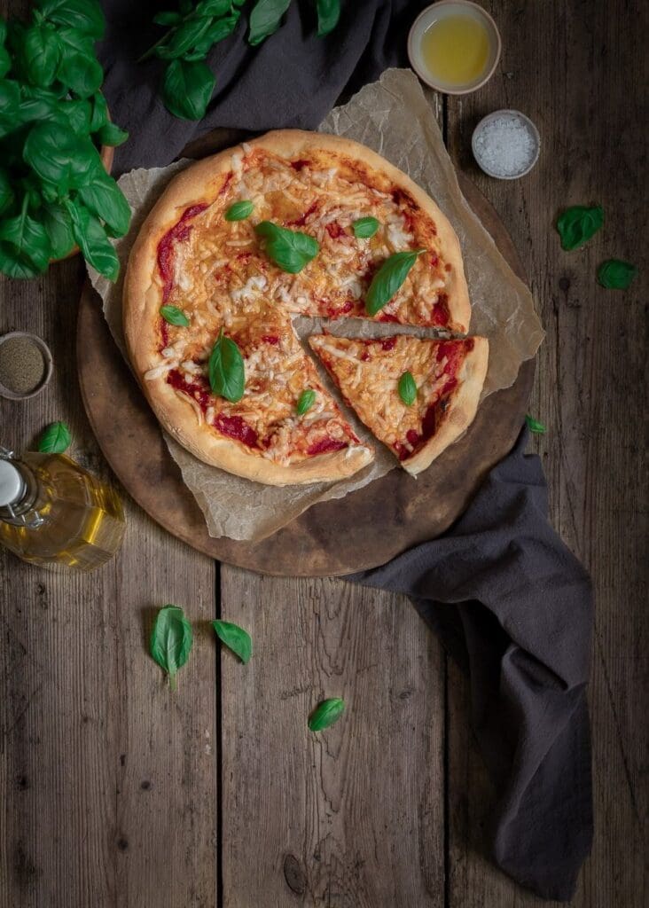 Freshly baked homemade pizza with rich tomato sauce, melted vegan cheese and fresh basil leaves on a rustic wooden table top. Using 48 hour pizza dough.