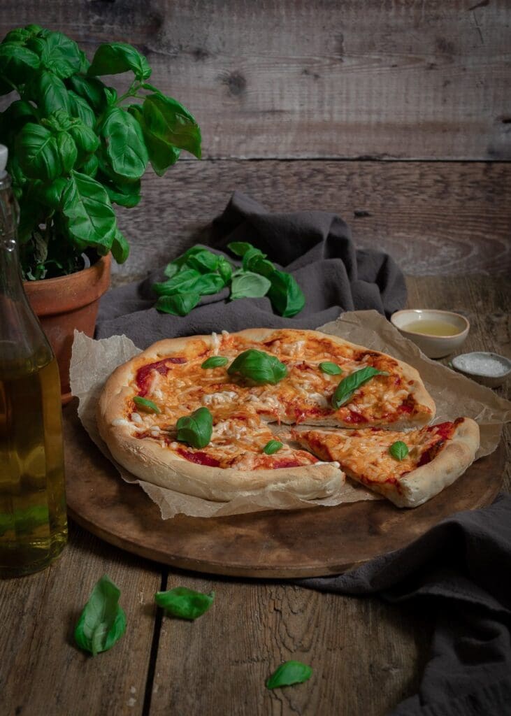 Freshly baked homemade pizza with rich tomato sauce, melted vegan cheese and fresh basil leaves on a rustic wooden table top. Using 48 hour pizza dough.
