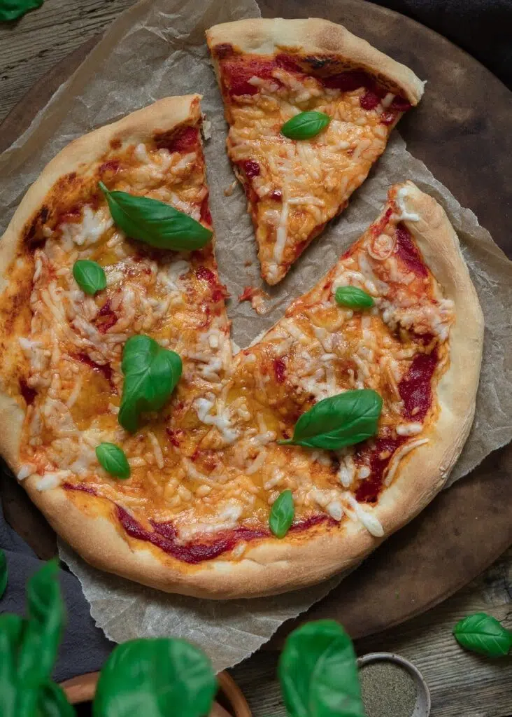 Freshly baked homemade pizza with rich tomato sauce, melted vegan cheese and fresh basil leaves on a rustic wooden table top