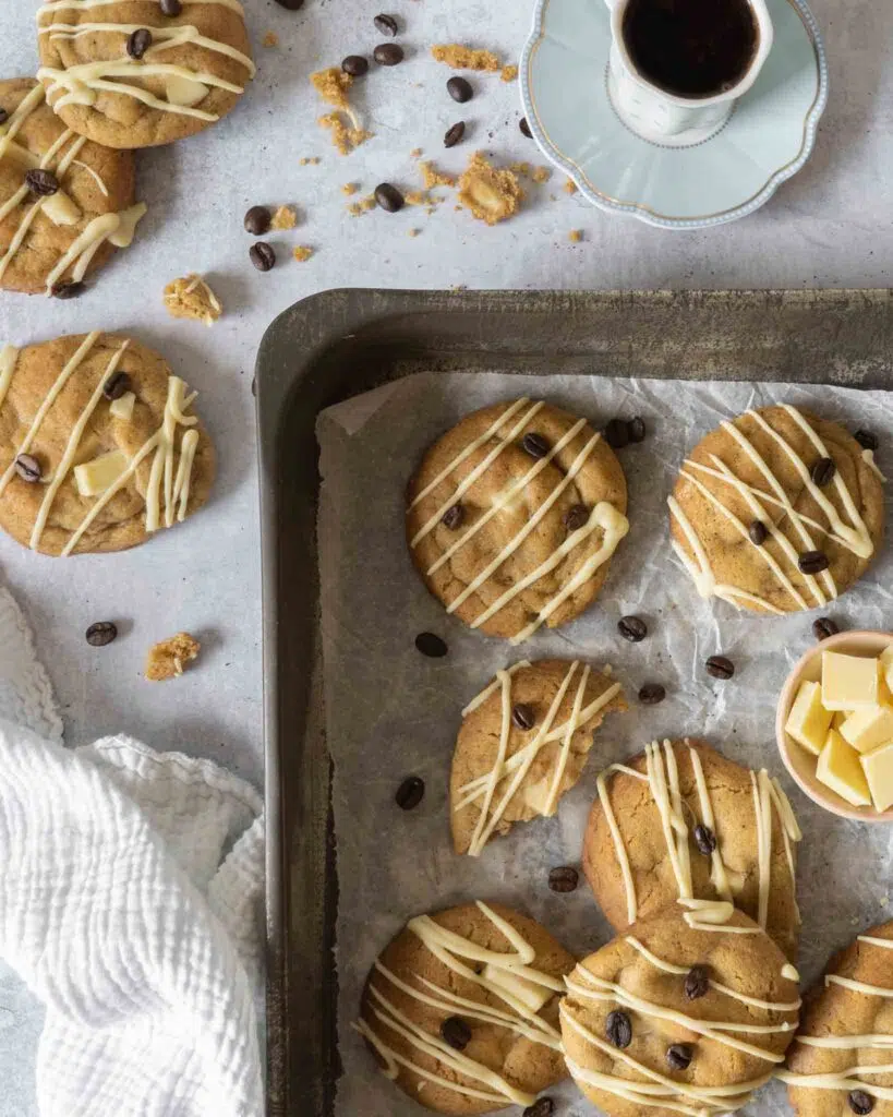 Vegan espresso martini cookies in a baking pan lined with parchment paper.  The cookies are drizzled with vegan white chocolate and decorated with coffee beans.