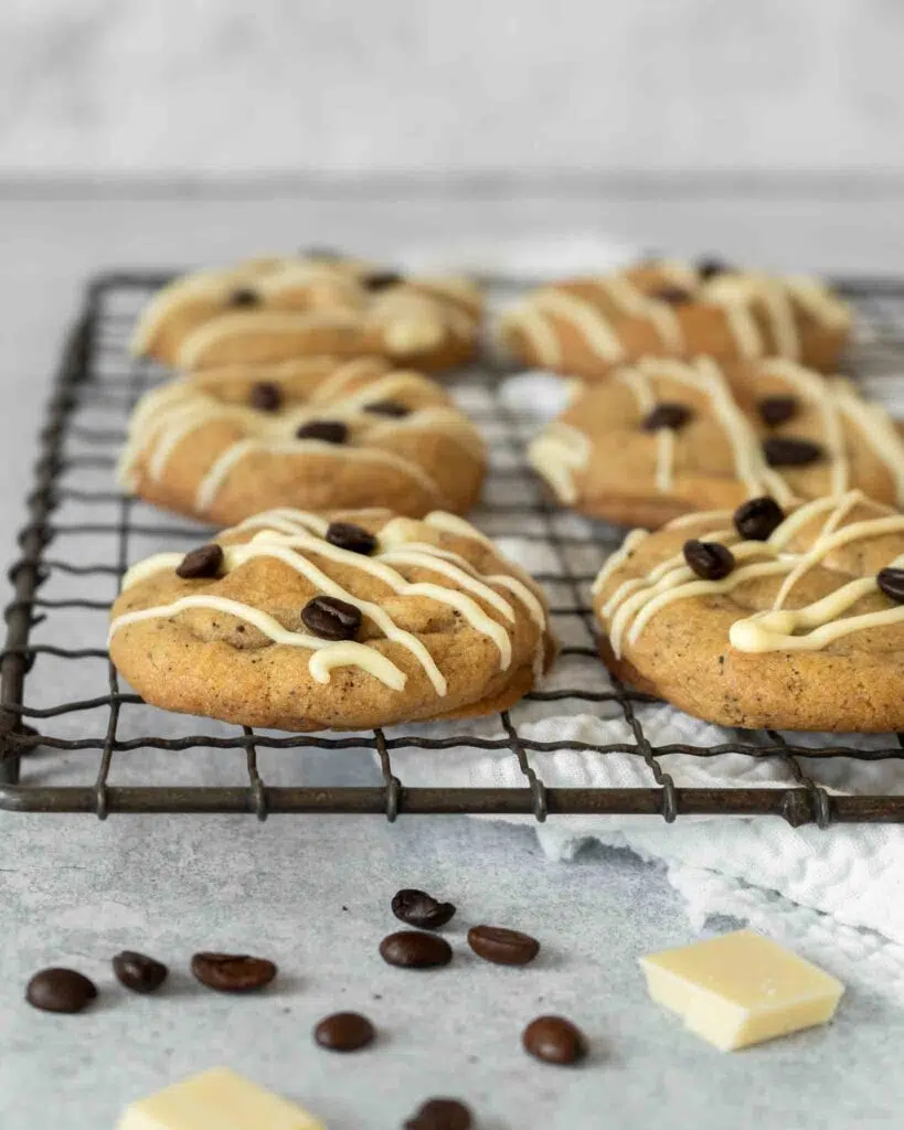 Chunky Espresso Martini Cookies resting on a cooling rack, drizzled with vegan white chocolate and decorated with coffee beans.