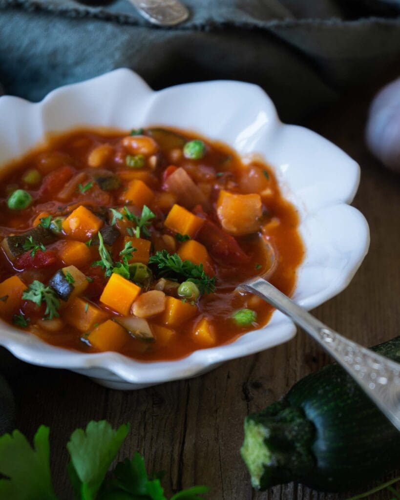 A bowl of colourful farmhouse vegetable soup on a rustic wooden farmhouse table with fresh ingredients surrounding it