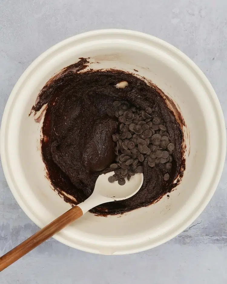 Adding chocolate chips to vegan brownie cake batter in a large mixing bowl