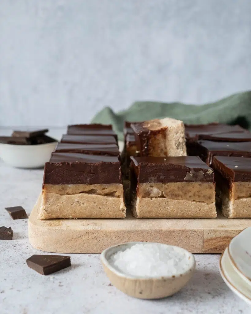 Healthy millionaire's shortbread slices on a wooden board with layers of sweet biscuit, date caramel and glossy dark chocolate
