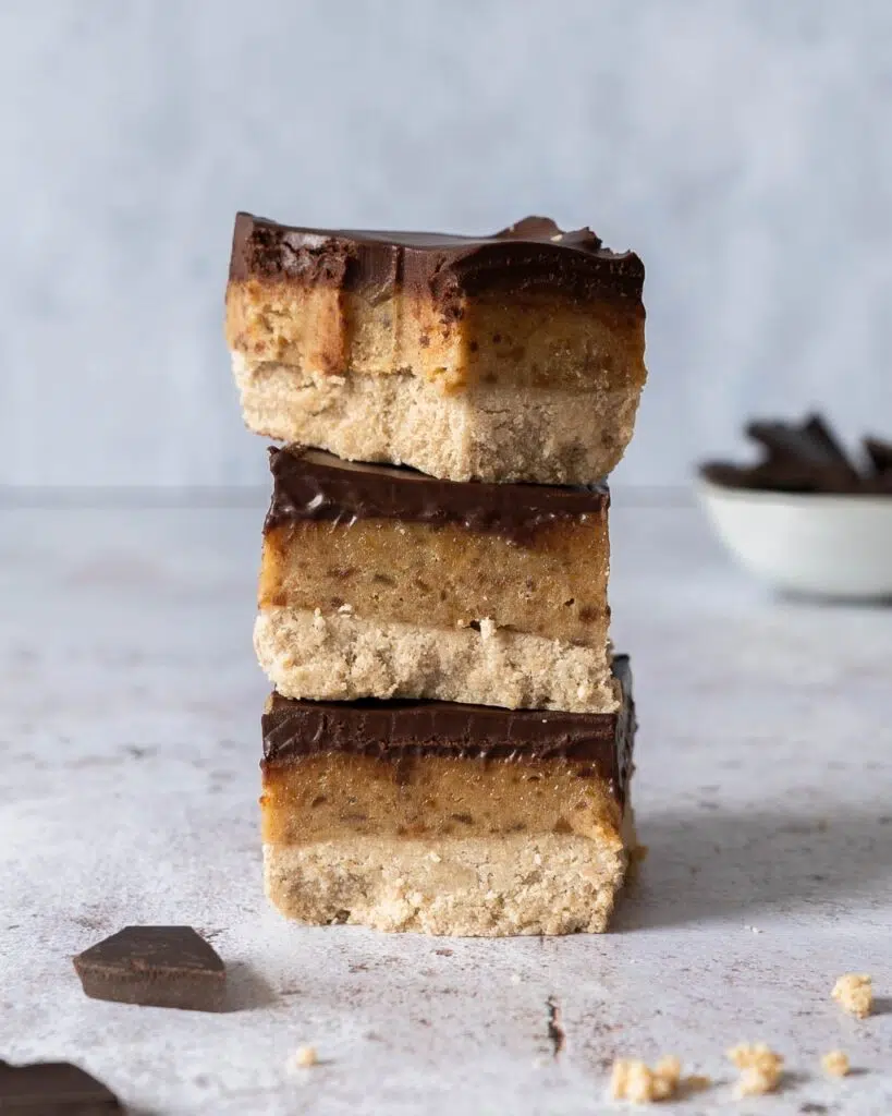 A stack of healthy millionaire's shortbread slices with layers of sweet biscuit, date caramel and glossy dark chocolate
