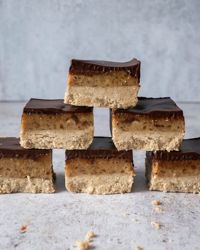 A stack of healthy millionaire's shortbread slices with layers of sweet biscuit, date caramel and glossy dark chocolate