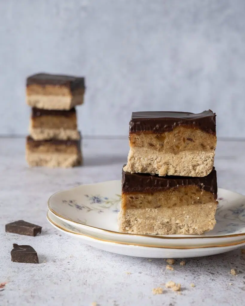 A stack of healthy millionaire's shortbread slices with layers of sweet biscuit, date caramel and glossy dark chocolate