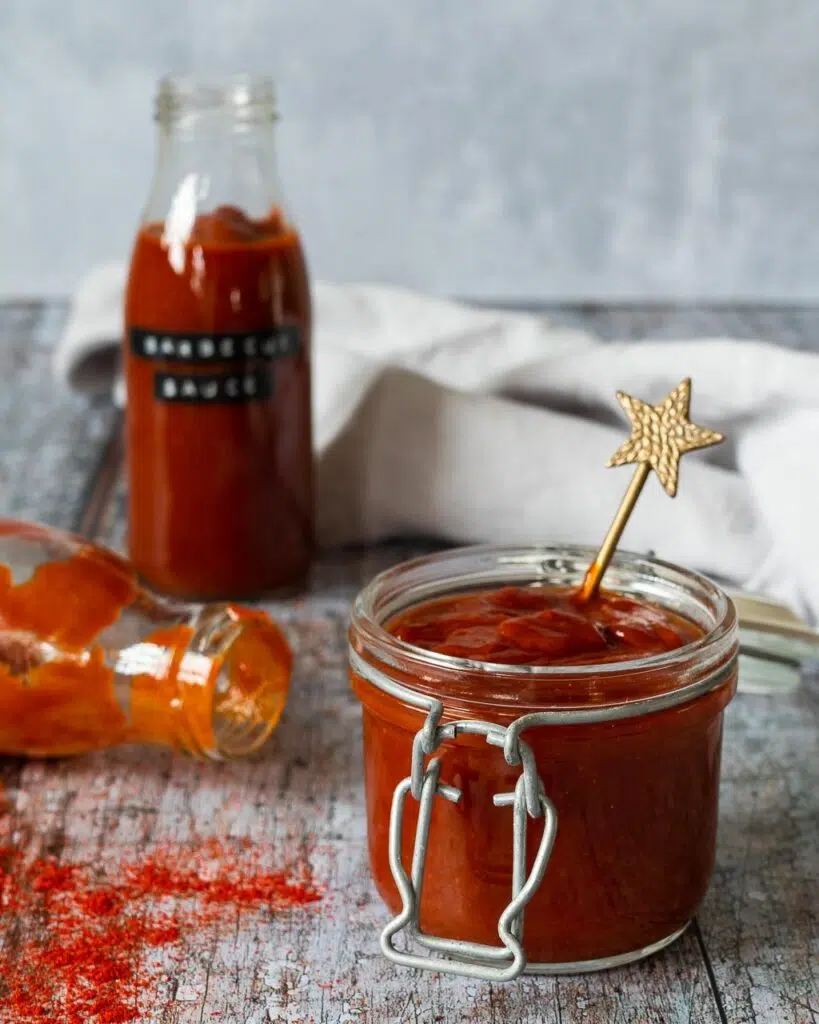 A glass jar filled with homemade BBQ sauce with a gold star spoon sticking out