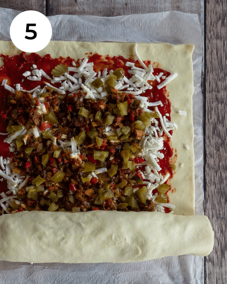 Puff pastry topped with tomato sauce, vegan cheese and Mexican spiced vegetables, being rolled up into a log