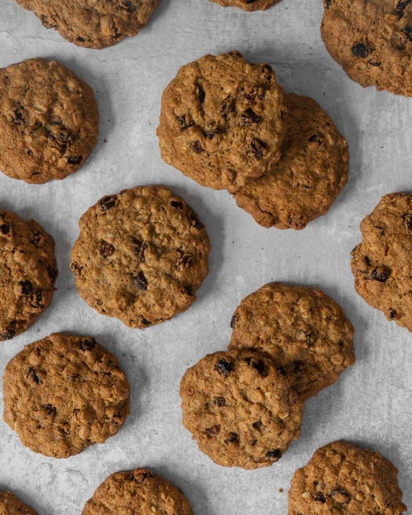 Cinnamon oat raisin cookies laid out on a table top, studded with juicy raisins
