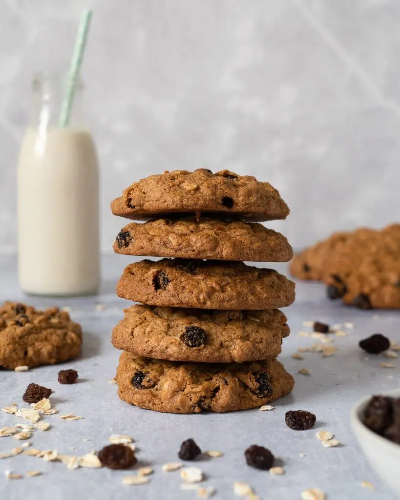 A stack of cinnamon oat raisin cookies on a table top with a miniature bottle of oat milk in the background