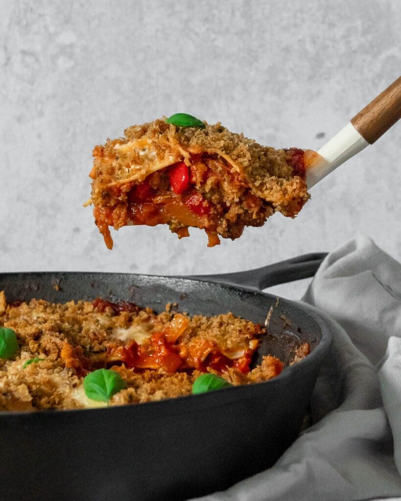 A single slice of One Pan Vegetable Lasagne being lifted out of the baking dish, with layers of pasta and colourful veggies on display.
