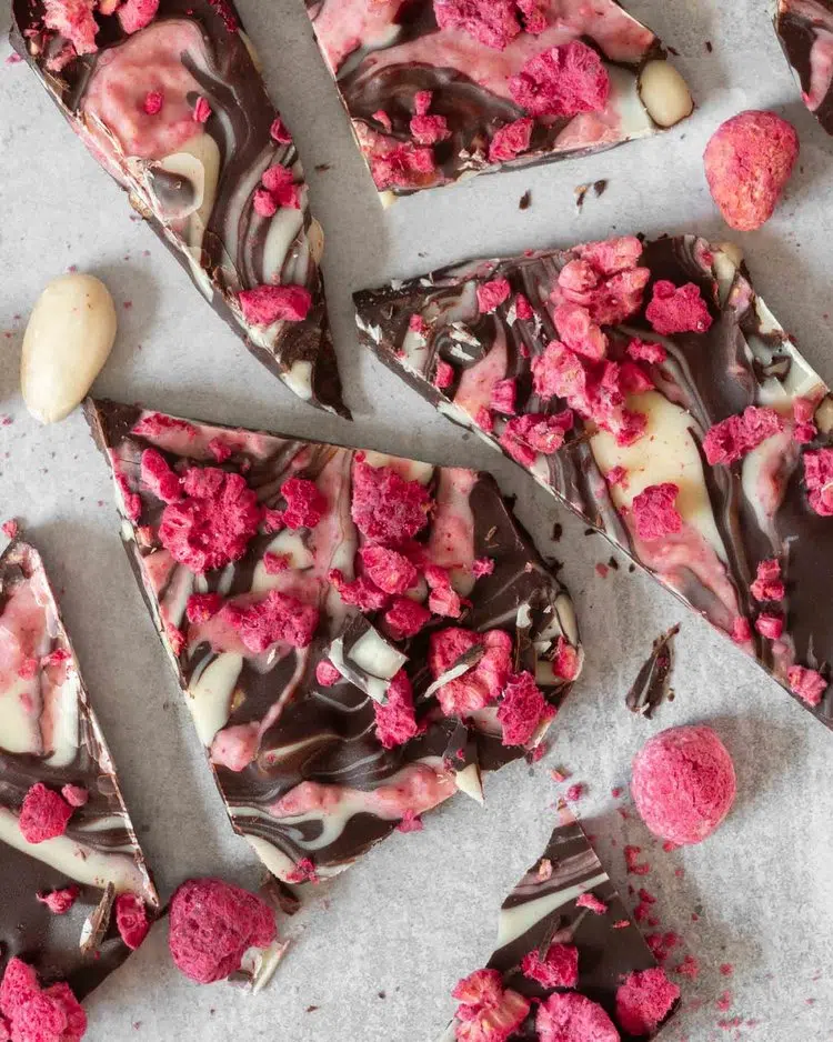 Chunky shards of dark chocolate with swirls of white and pink raspberry chocolate and bright pink freeze dried raspberries and white blanched almonds sprinkled on top