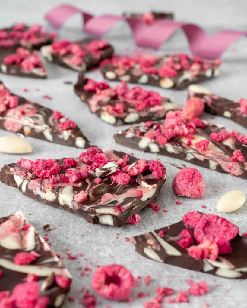 Chunky shards of dark chocolate with swirls of white and pink raspberry chocolate and bright pink freeze dried raspberries and white blanched almonds sprinkled on top