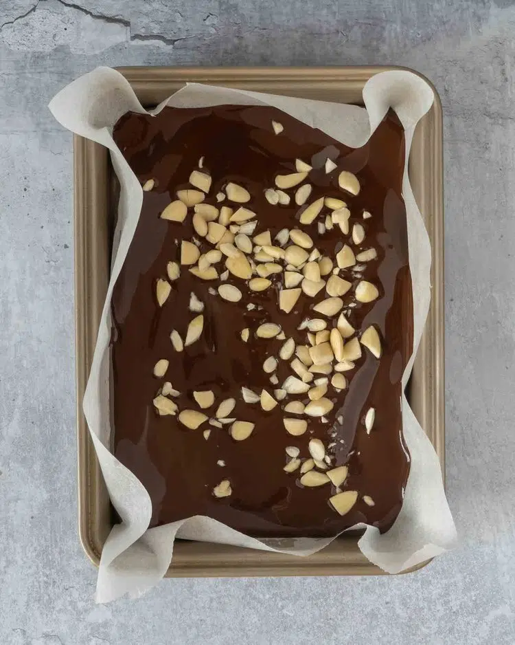 Melted dark chocolate in a brownie tin lined with baking paper, with chopped blanched almonds sprinkled on top