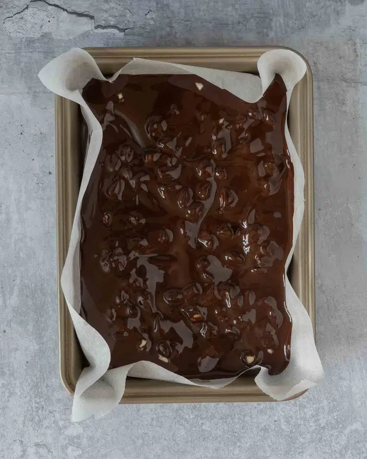 Melted dark chocolate in a baking tray lined with parchment paper, with chopped almonds stirred through