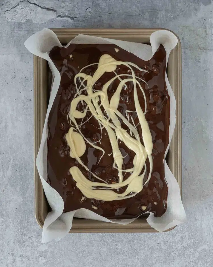 Melted dark chocolate in a lined baking tray with melted white chocolate swirled on top