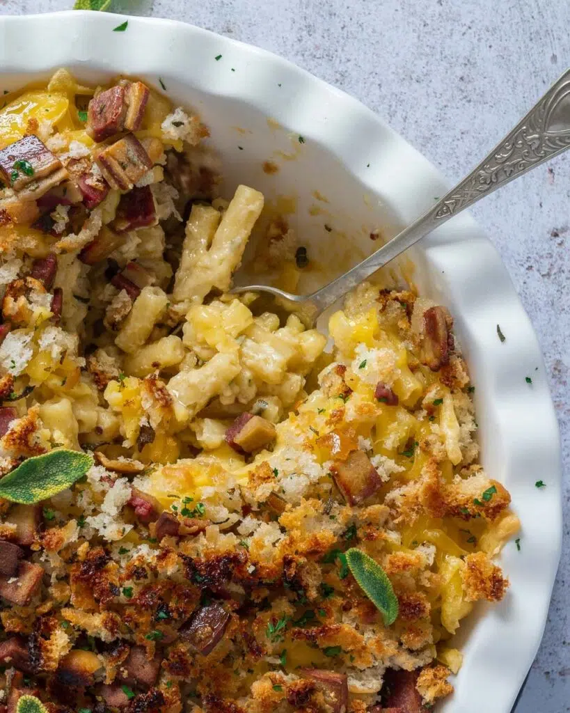 A baking dish filled with creamy vegan Mac n cheese, topped with breadcrumbs, vegan bacon and fresh sage leaves