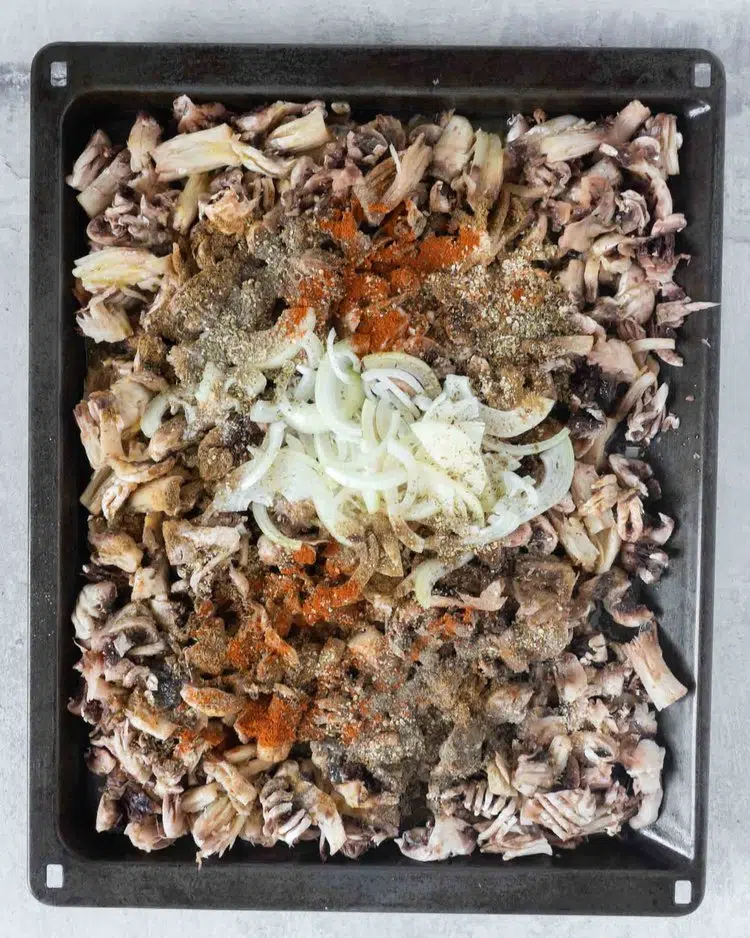 Shredded mushrooms on an oven tray topped with sliced onions and spices
