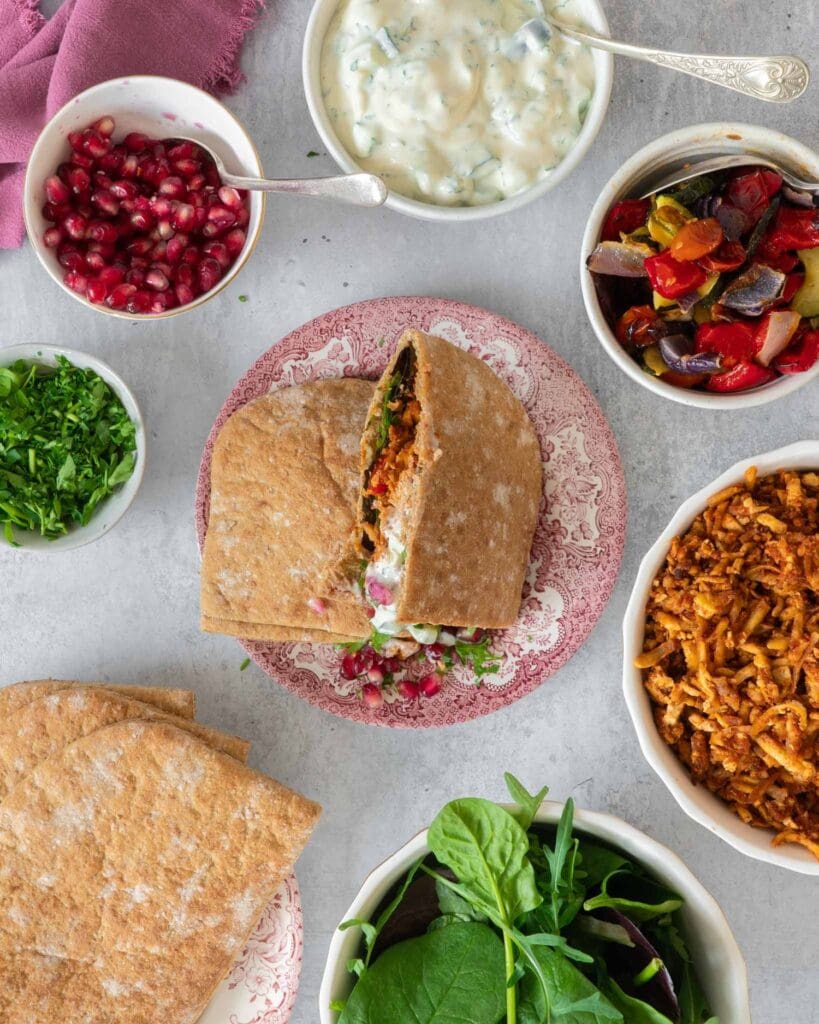 Open pitta breads stuffed with spiced shredded tofu kebab 'meat', roasted vegetables, glistening pomegranate seeds, creamy fresh tzatziki and rocket