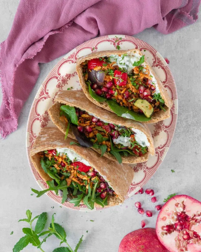 Open pitta breads stuffed with spiced shredded tofu kebab 'meat', roasted vegetables, glistening pomegranate seeds, creamy fresh tzatziki and rocket
