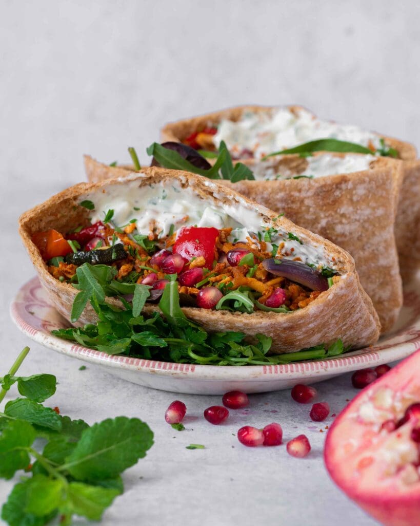 Open pitta breads stuffed with spiced shredded tofu kebab 'meat', roasted vegetables, glistening pomegranate seeds, creamy fresh tzatziki and rocket