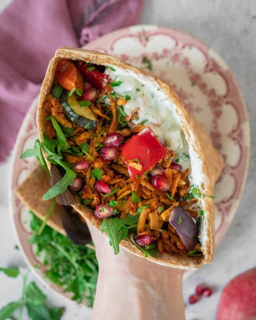 Open pitta breads stuffed with spiced shredded tofu kebab 'meat', roasted vegetables, glistening pomegranate seeds, creamy fresh tzatziki and rocket