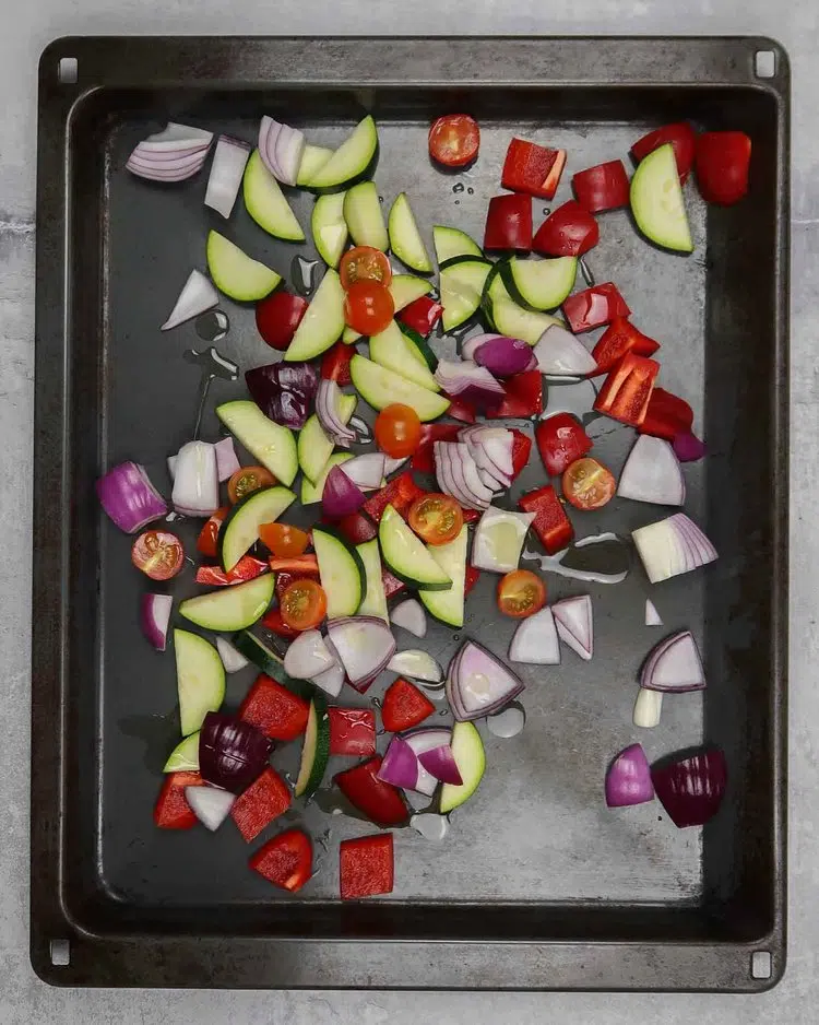Courgette slices, red onion chunks, red pepper cubes and cherry tomatoes on a roasting tray drizzled in olive oil