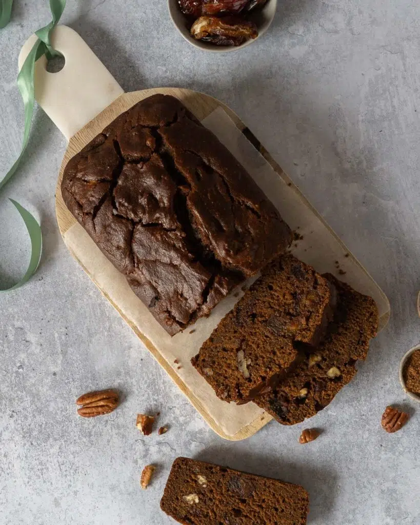 A rich sticky date cake on a wooden chopping board with two slices cut
