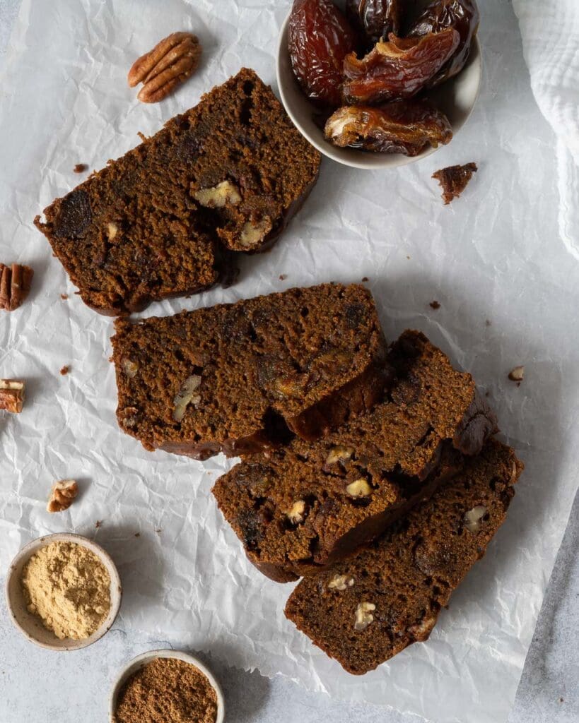 Slices of a rich sticky date cake on a table top covered with baking paper