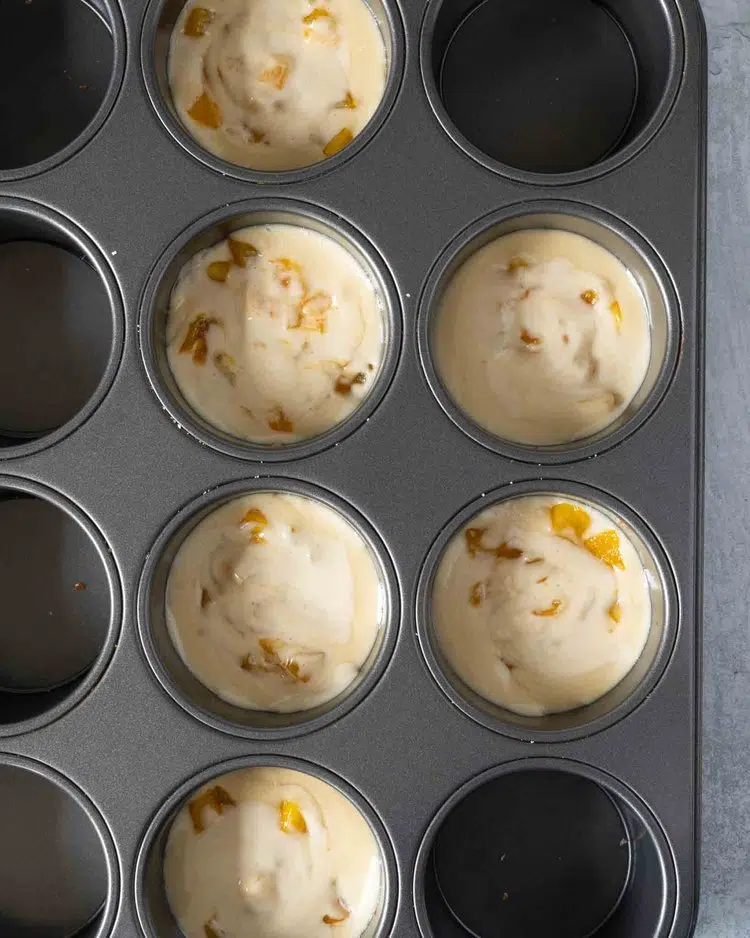 Mini vegan cheesecakes in a muffin tin with sticky mango pieces stirred through to create a marbling effect