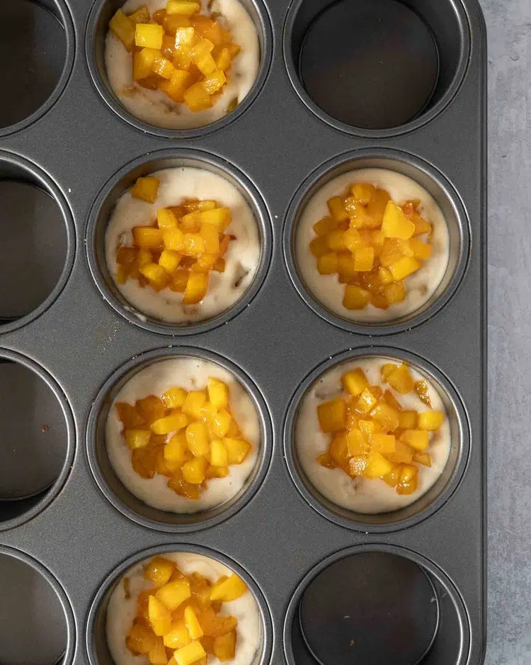 Individual vegan cheesecakes in a muffin tin topped with sticky mango pieces