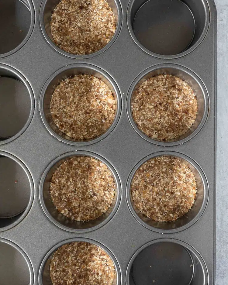 A muffin tin filled with an oat mix to make the base of individual cheesecakes