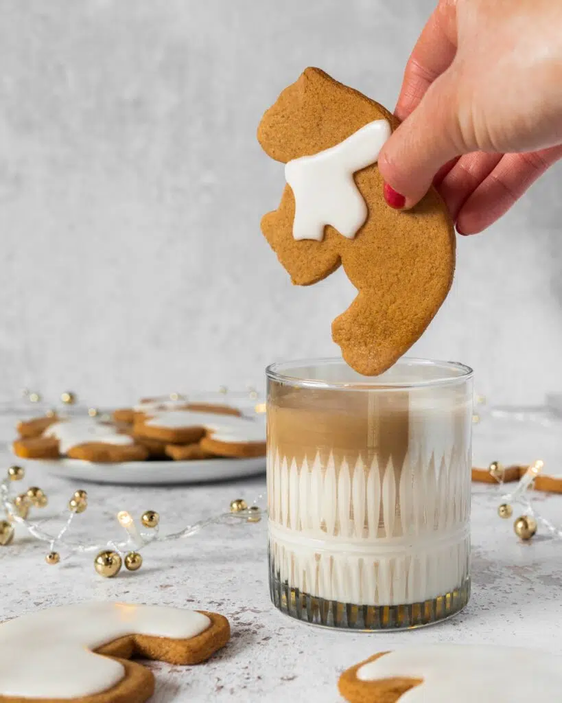 A gingerbread bear cookie being dunked in a glass of dairy free milk