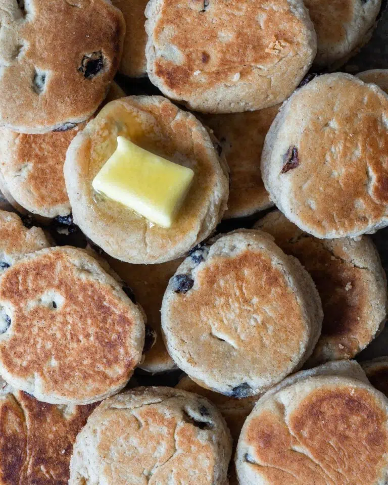 A table full of round vegan welsh cakes studded with juicy sultanas and topped with melting vegan butter
