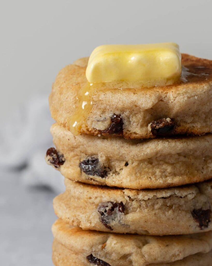A stack of chunky round vegan welsh cakes studded with juicy sultanas and topped with melting vegan butter